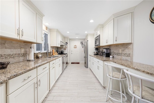 kitchen with light stone counters, appliances with stainless steel finishes, white cabinetry, and sink