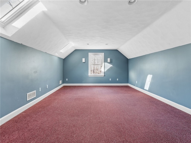 additional living space with a textured ceiling, vaulted ceiling with skylight, and carpet