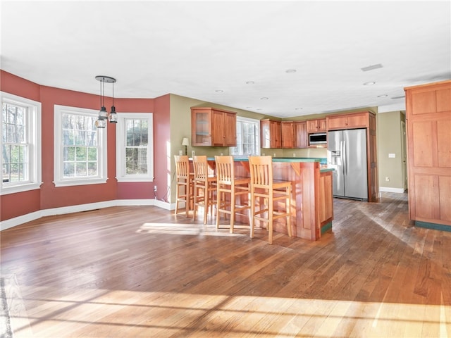 kitchen with hardwood / wood-style flooring, pendant lighting, stainless steel appliances, a notable chandelier, and a kitchen breakfast bar