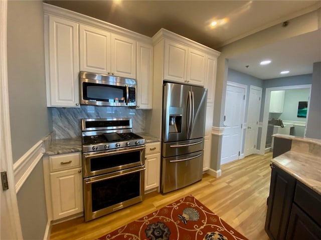 kitchen with appliances with stainless steel finishes, light hardwood / wood-style floors, light stone countertops, white cabinets, and backsplash