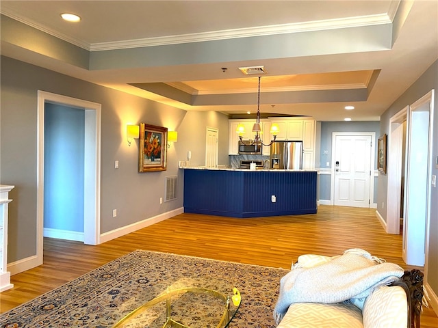 living room with ornamental molding, light hardwood / wood-style floors, a tray ceiling, and a notable chandelier