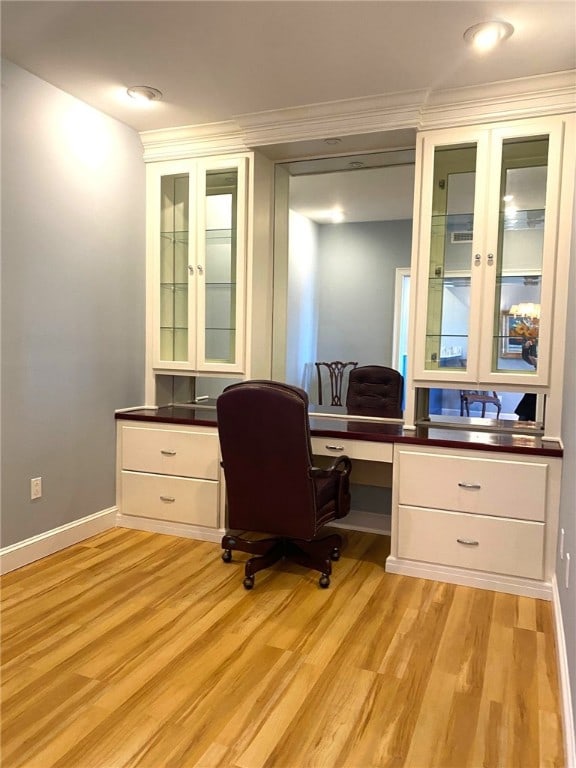 office with light wood-type flooring, crown molding, and built in desk