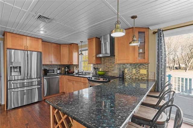 kitchen featuring appliances with stainless steel finishes, hanging light fixtures, wall chimney range hood, and kitchen peninsula