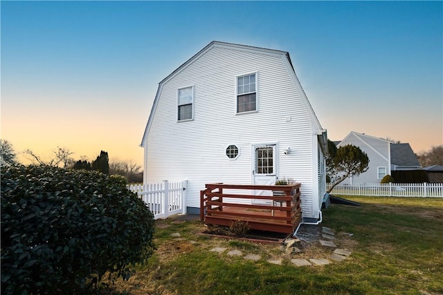 back house at dusk featuring a deck and a lawn