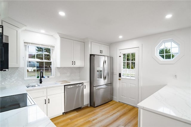 kitchen featuring appliances with stainless steel finishes, white cabinetry, tasteful backsplash, sink, and light hardwood / wood-style flooring