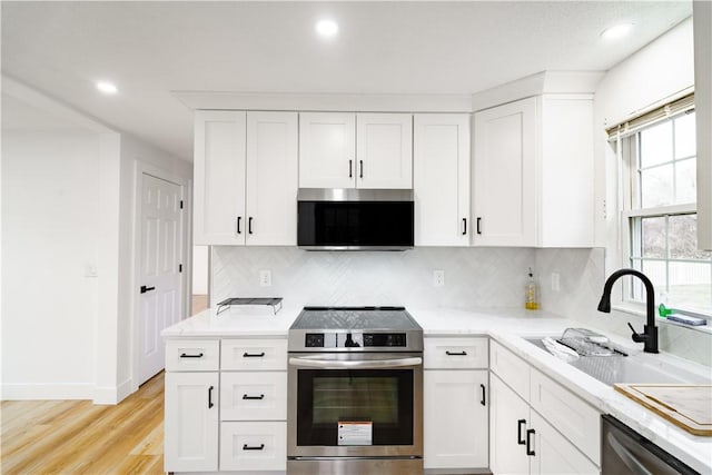 kitchen with white cabinets, stainless steel appliances, tasteful backsplash, light hardwood / wood-style floors, and sink