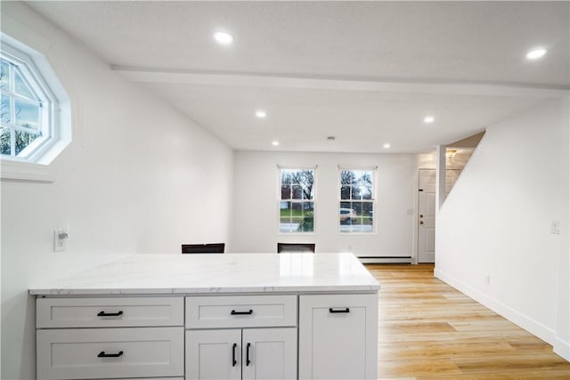 kitchen with a wealth of natural light, light stone counters, white cabinetry, and a baseboard radiator