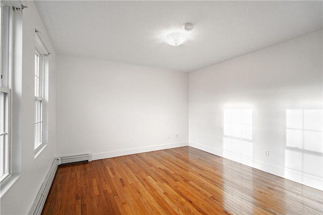 empty room featuring a baseboard heating unit, a wealth of natural light, and hardwood / wood-style flooring