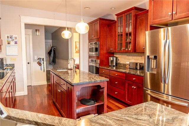 kitchen with sink, decorative light fixtures, light stone counters, stainless steel refrigerator with ice dispenser, and a kitchen island with sink