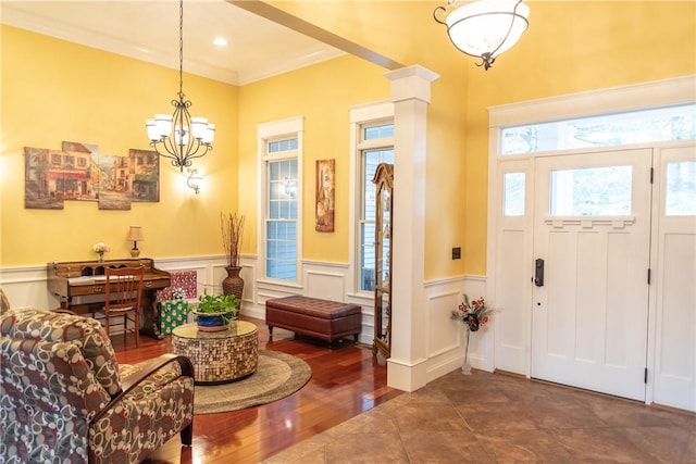 foyer featuring a notable chandelier, decorative columns, hardwood / wood-style flooring, and crown molding