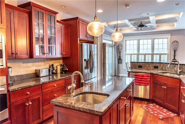 kitchen with sink, an island with sink, coffered ceiling, and appliances with stainless steel finishes