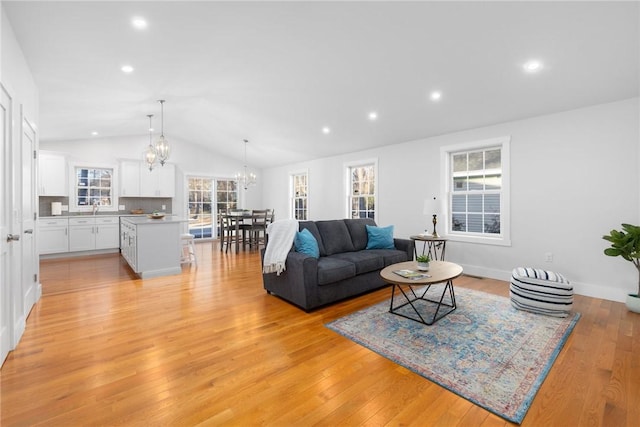 living room with sink, vaulted ceiling, a chandelier, and light hardwood / wood-style floors