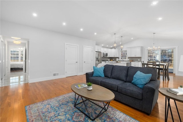 living room with vaulted ceiling, light hardwood / wood-style flooring, and an inviting chandelier