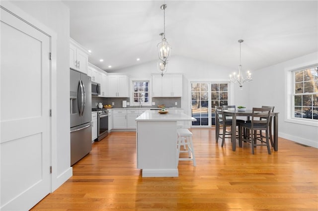 kitchen featuring vaulted ceiling, white cabinetry, decorative backsplash, a kitchen island, and stainless steel appliances