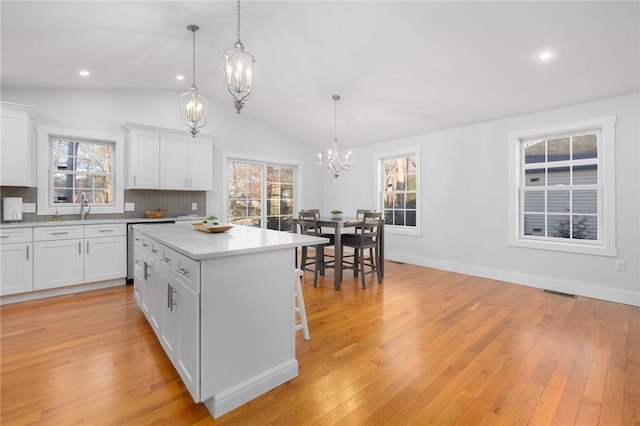 kitchen with hanging light fixtures, white cabinets, a kitchen island, and tasteful backsplash