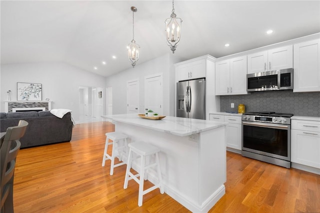 kitchen with white cabinets, appliances with stainless steel finishes, hanging light fixtures, vaulted ceiling, and a breakfast bar