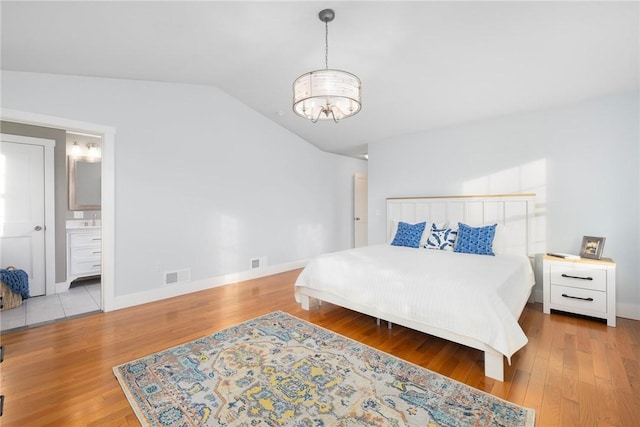 bedroom featuring lofted ceiling, light wood-type flooring, a notable chandelier, and ensuite bathroom