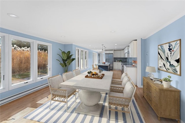 dining room featuring light hardwood / wood-style floors, baseboard heating, and crown molding