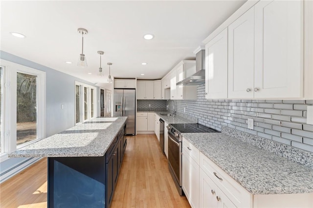 kitchen with stainless steel appliances, a center island, wall chimney exhaust hood, white cabinetry, and decorative light fixtures