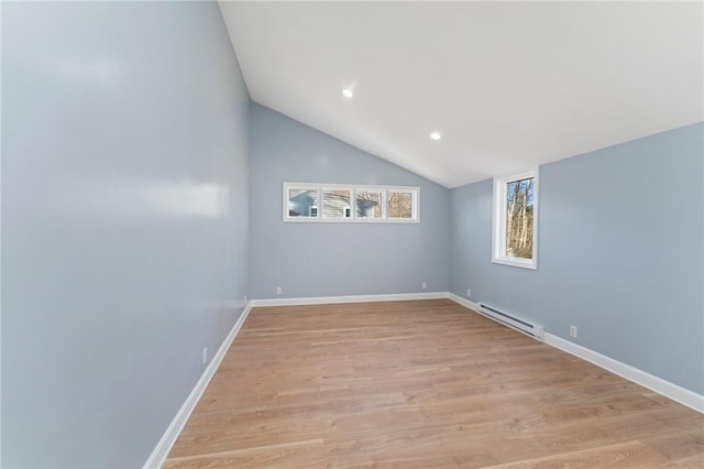 empty room featuring light hardwood / wood-style floors, a baseboard heating unit, and vaulted ceiling