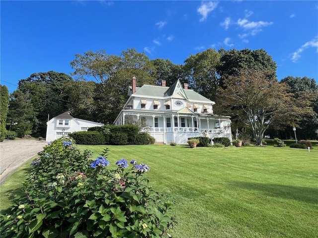 view of front of home with covered porch, a chimney, and a front yard