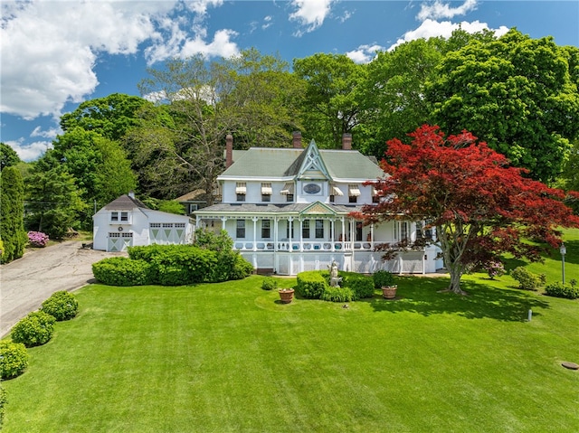 view of front of home featuring a front yard, covered porch, an outdoor structure, and a chimney