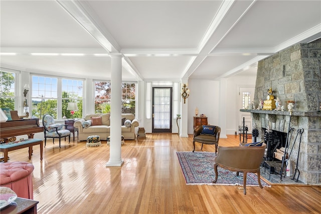 sitting room featuring light wood-type flooring, beam ceiling, a stone fireplace, and ornate columns