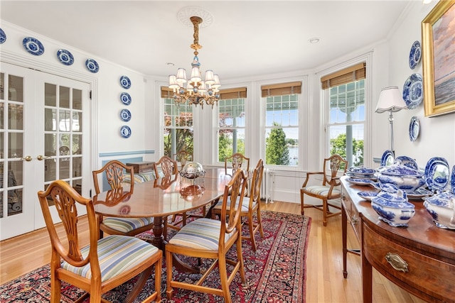 dining room featuring light wood-style flooring, a chandelier, crown molding, and french doors