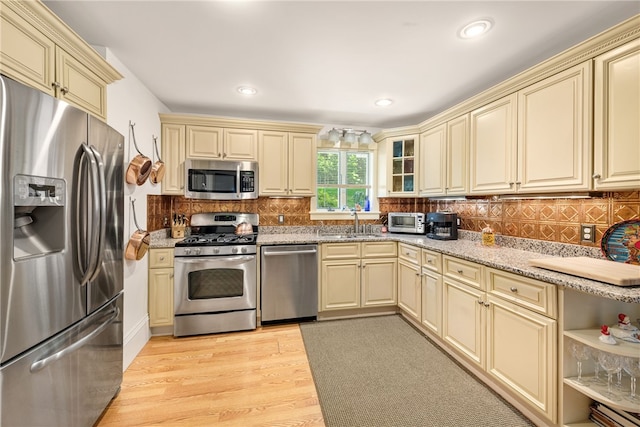 kitchen with light wood finished floors, cream cabinetry, backsplash, and appliances with stainless steel finishes