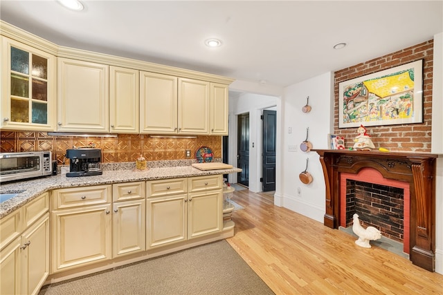 kitchen featuring light stone counters, a toaster, tasteful backsplash, cream cabinets, and light wood-type flooring