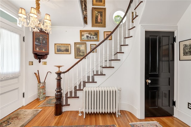 foyer featuring wood finished floors, baseboards, stairs, radiator heating unit, and an inviting chandelier