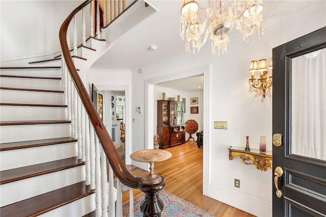 entrance foyer featuring a notable chandelier, ornamental molding, wood finished floors, baseboards, and stairs