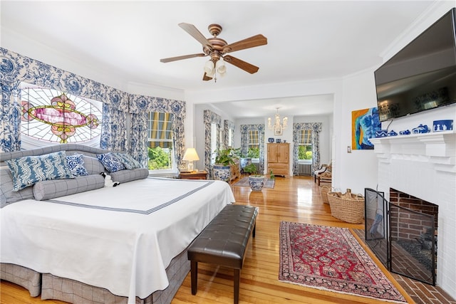 bedroom featuring crown molding, a fireplace, wood finished floors, and ceiling fan with notable chandelier