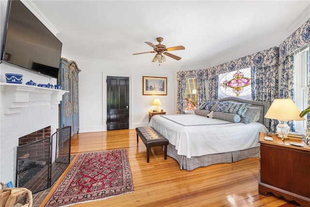 bedroom with baseboards, a ceiling fan, ornamental molding, wood finished floors, and a fireplace