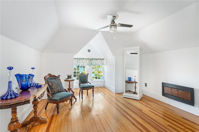 living area with baseboards, a glass covered fireplace, lofted ceiling, wood-type flooring, and ceiling fan