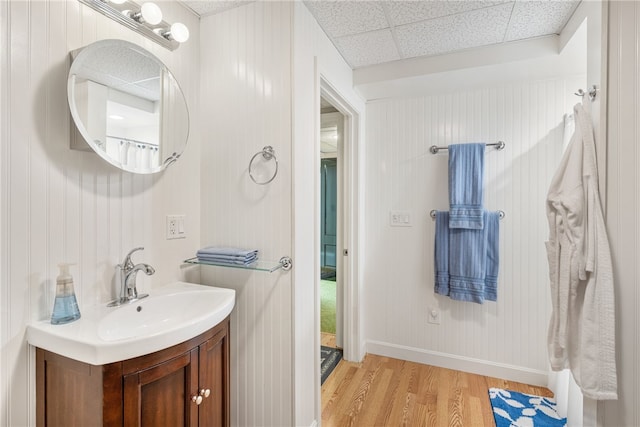 bathroom featuring vanity, wood finished floors, a paneled ceiling, and baseboards