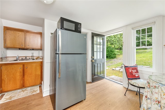 kitchen with light wood-type flooring, a sink, freestanding refrigerator, and brown cabinets