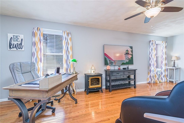 home office featuring wood-type flooring, ceiling fan, and a wood stove