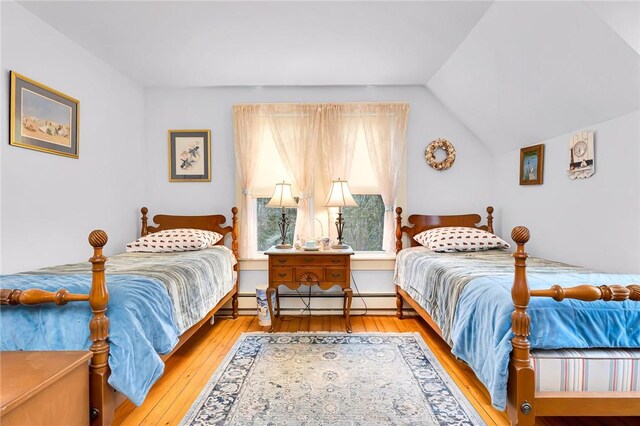 bedroom with vaulted ceiling, light wood-type flooring, and a baseboard radiator