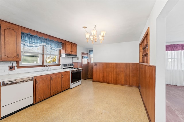 kitchen featuring white appliances, a notable chandelier, wooden walls, and sink