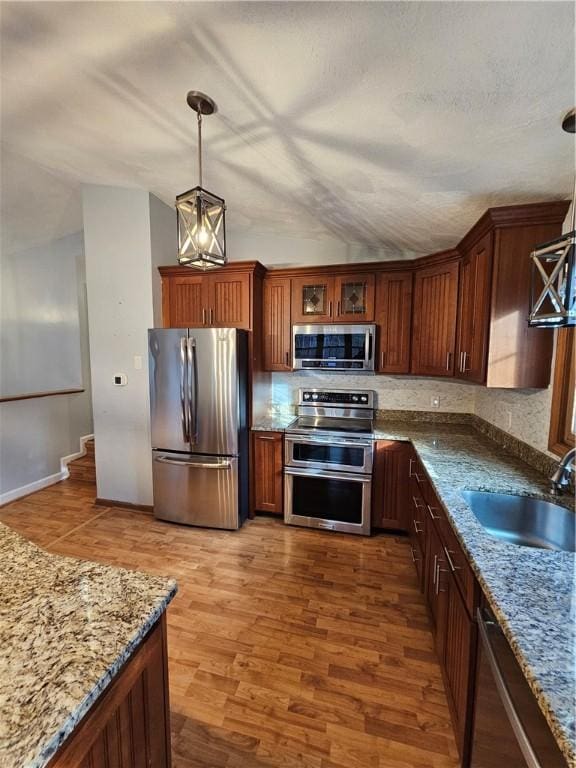 kitchen with stainless steel appliances, sink, light stone counters, hardwood / wood-style floors, and hanging light fixtures