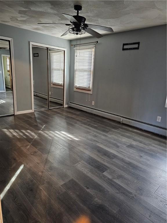 spare room featuring a baseboard heating unit, dark wood-type flooring, ceiling fan, and a textured ceiling