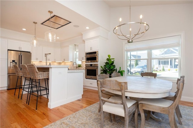 dining space with sink, crown molding, light hardwood / wood-style floors, and a notable chandelier