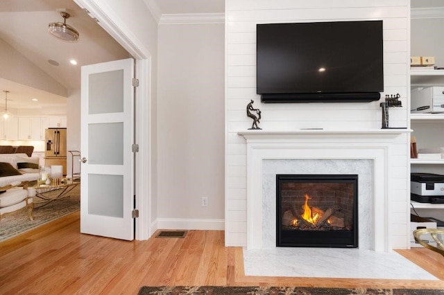 living room with lofted ceiling, a high end fireplace, light hardwood / wood-style floors, and ornamental molding