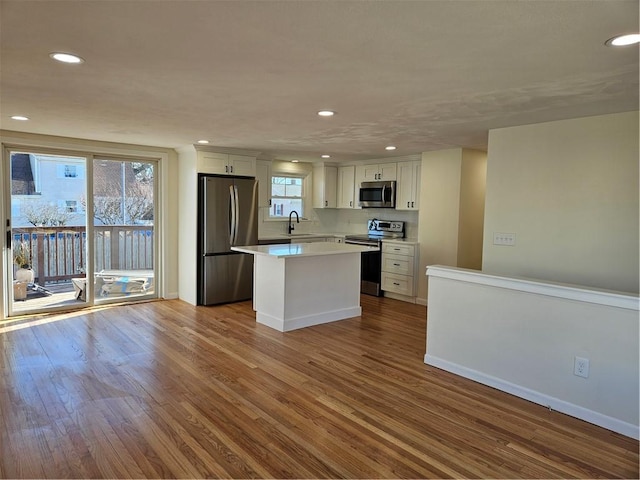 kitchen featuring wood-type flooring, appliances with stainless steel finishes, a center island, white cabinets, and sink