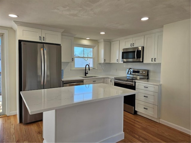 kitchen with light stone countertops, a center island, stainless steel appliances, white cabinets, and sink