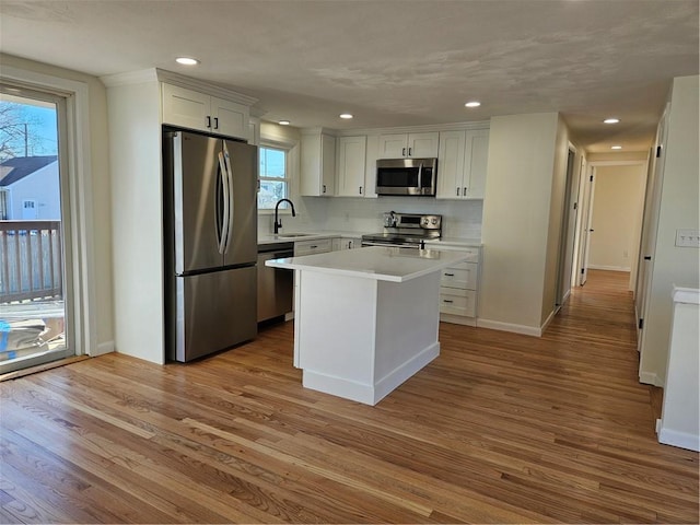 kitchen with sink, white cabinetry, light hardwood / wood-style floors, a kitchen island, and appliances with stainless steel finishes