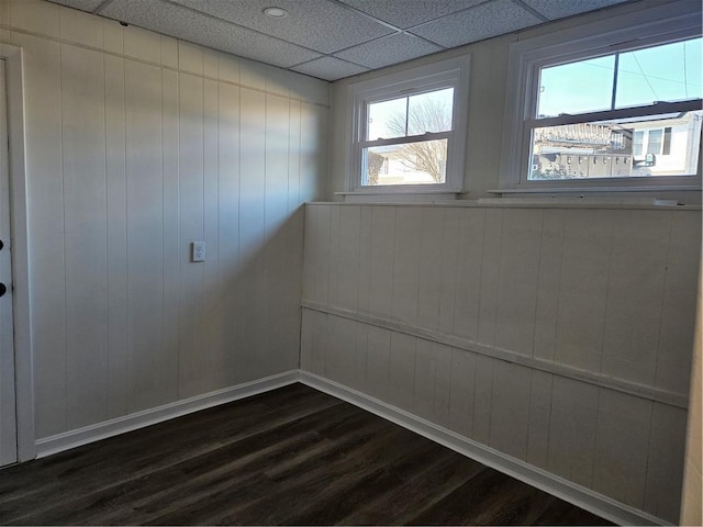 empty room featuring dark wood-type flooring, wooden walls, and a paneled ceiling