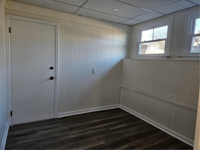 empty room featuring a paneled ceiling, dark hardwood / wood-style flooring, and wood walls