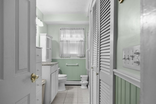 bathroom with toilet, vanity, a baseboard heating unit, tile patterned floors, and wood walls